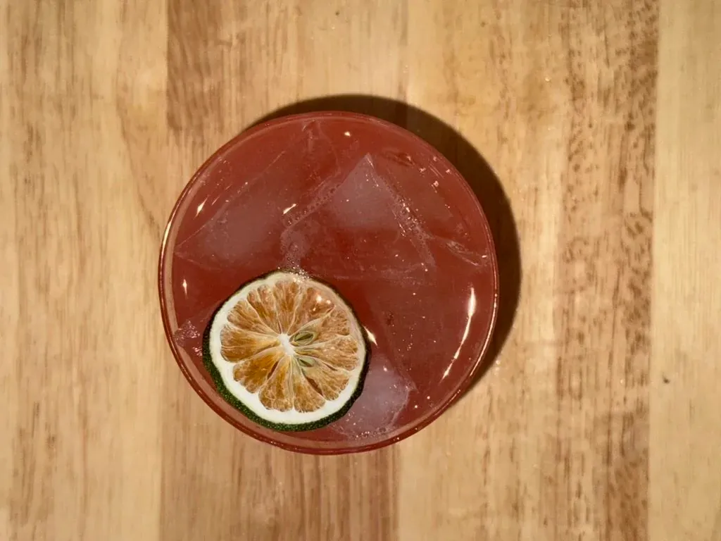 Bitter margarita in a rocks glass with a dehydrated lime wheel, shot from above on a butcher block