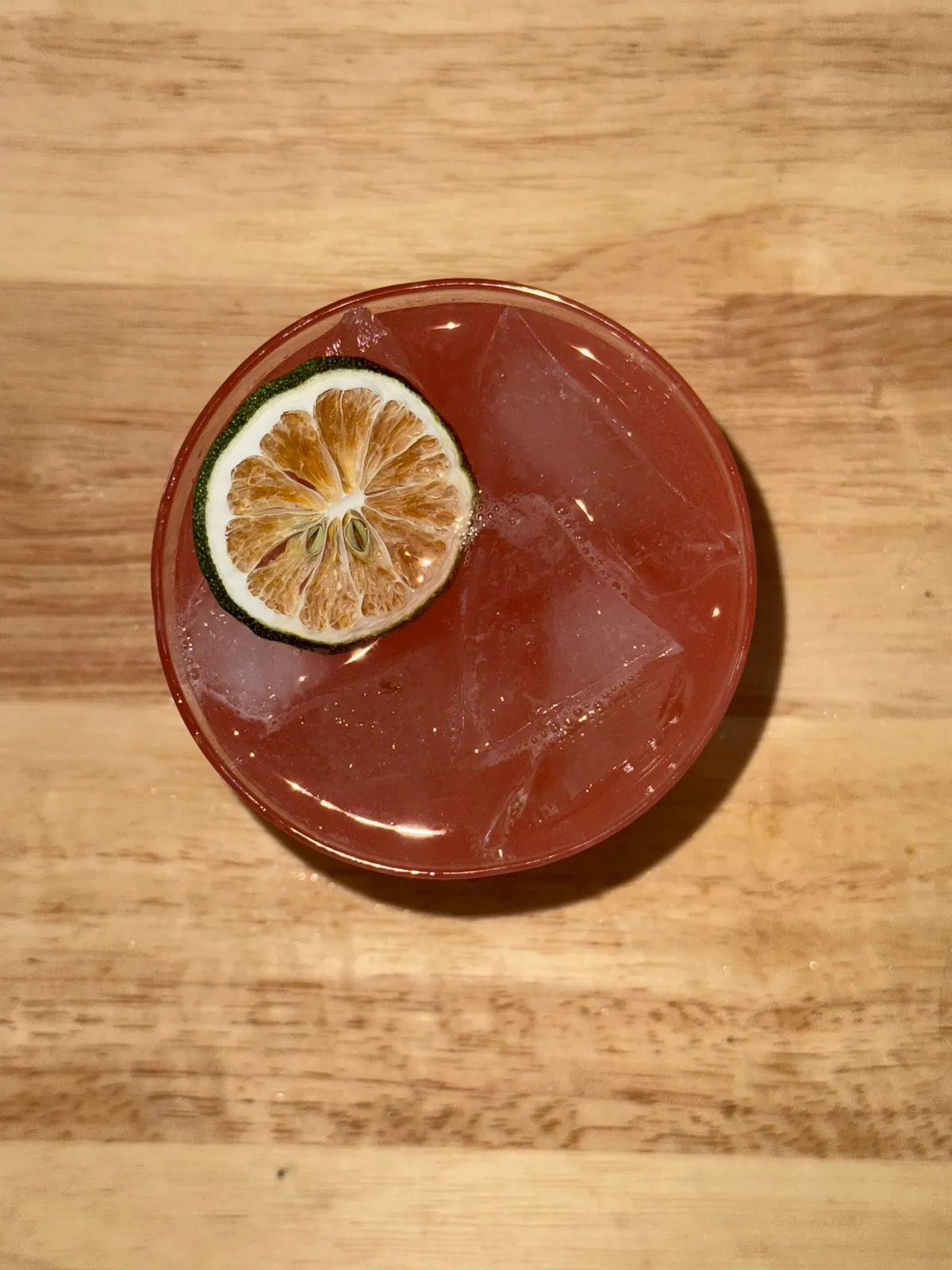Bitter margarita – deep red cocktail over a big cube in a rocks glass with a dehydrated lime wheel, shot from above on a butcher block