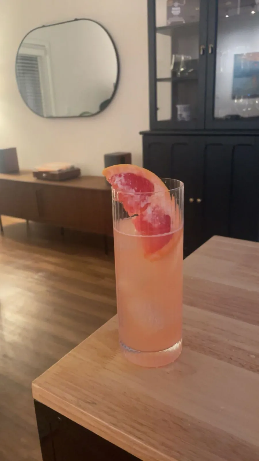 Old Salt – pale pink grapefruit highball in a fluted highball glass with an oversized salted grapefruit wedge, on a wood table